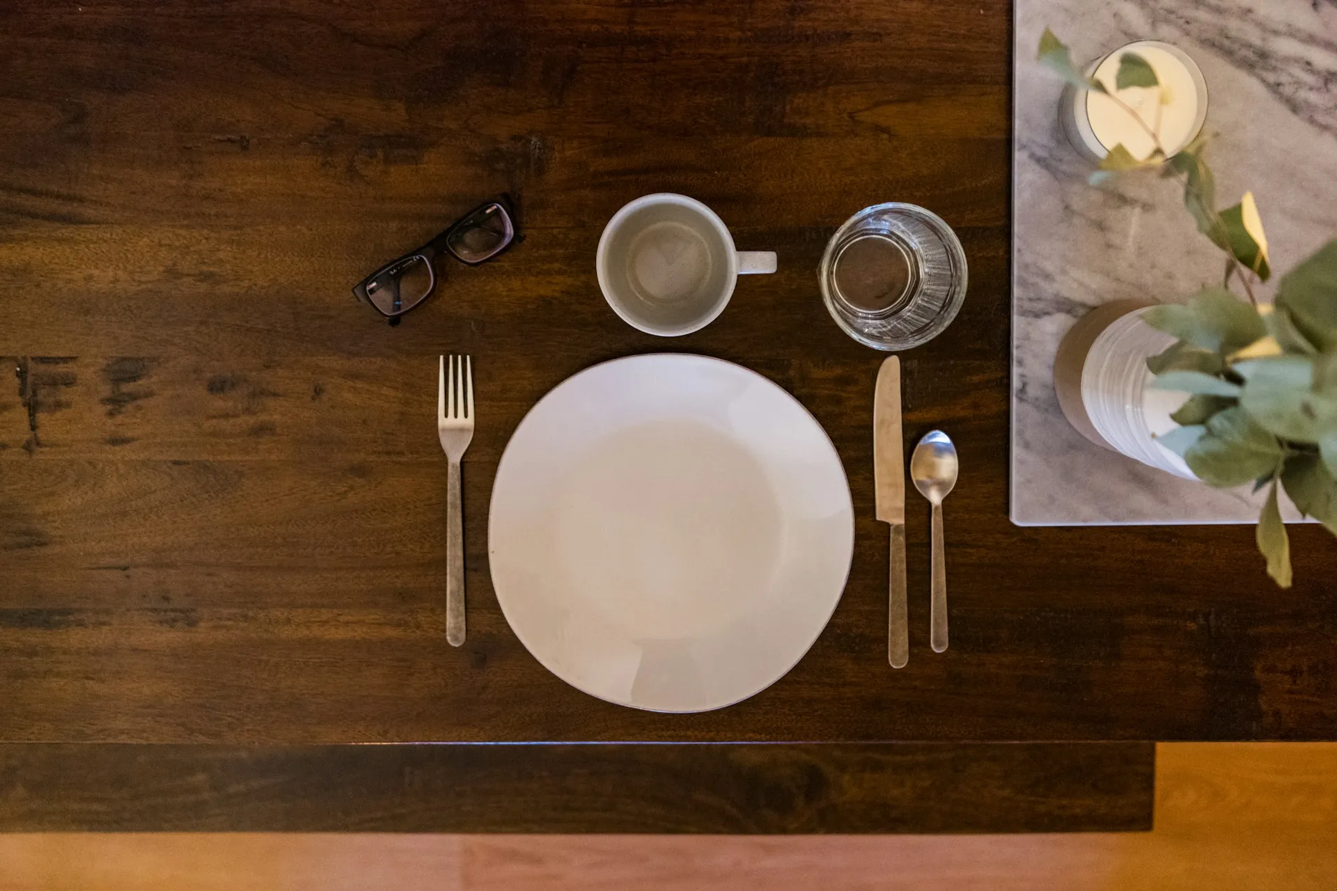 Two plated meals with wine glasses, bread and flowers on a white table outdoors overlooking a lawn