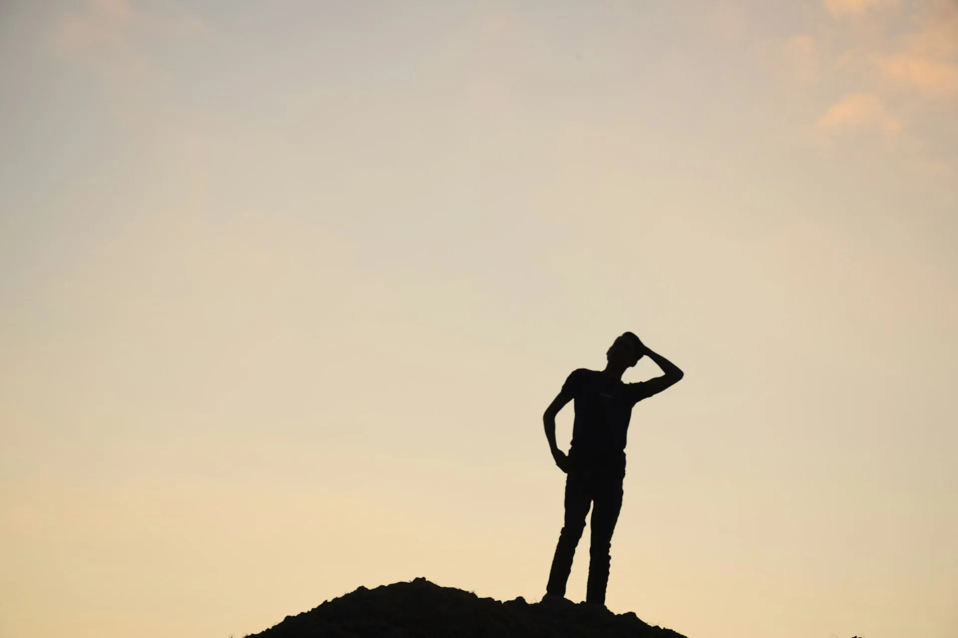 Silhouette of a person standing on a mound of earth against a pale sunset sky