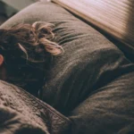 A person sleeping deeply under a blanket in a dimly lit room, showcasing the biological process of sleep recovery and circadian rhythm restoration.
