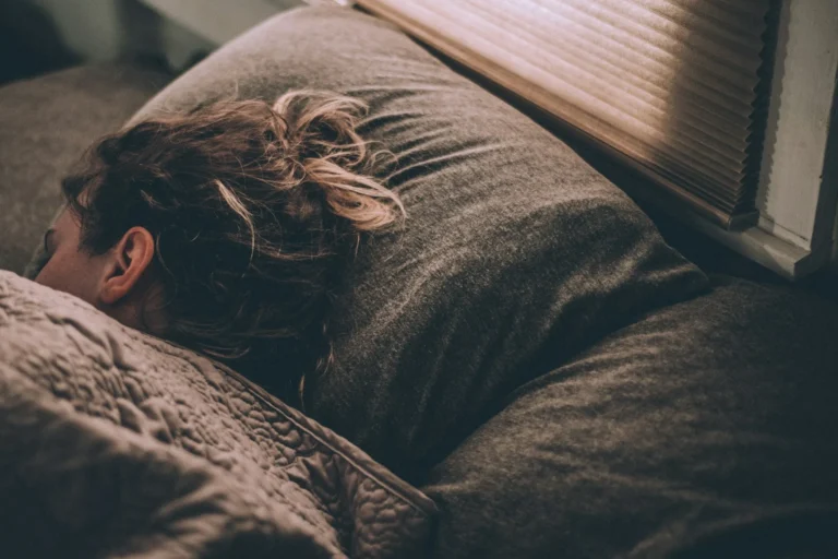 A person sleeping deeply under a blanket in a dimly lit room, showcasing the biological process of sleep recovery and circadian rhythm restoration.