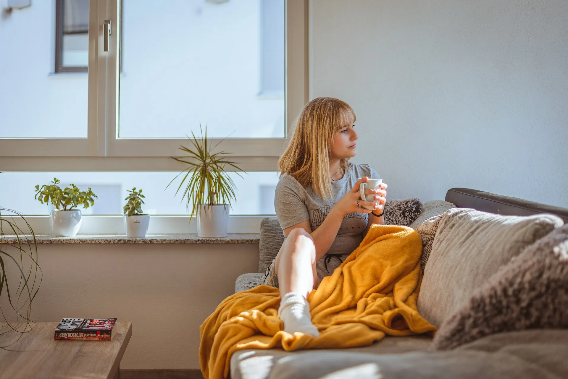 Woman relaxing peacefully on a couch with a warm drink looking out a window experiencing somatic safety and true nervous system reset.