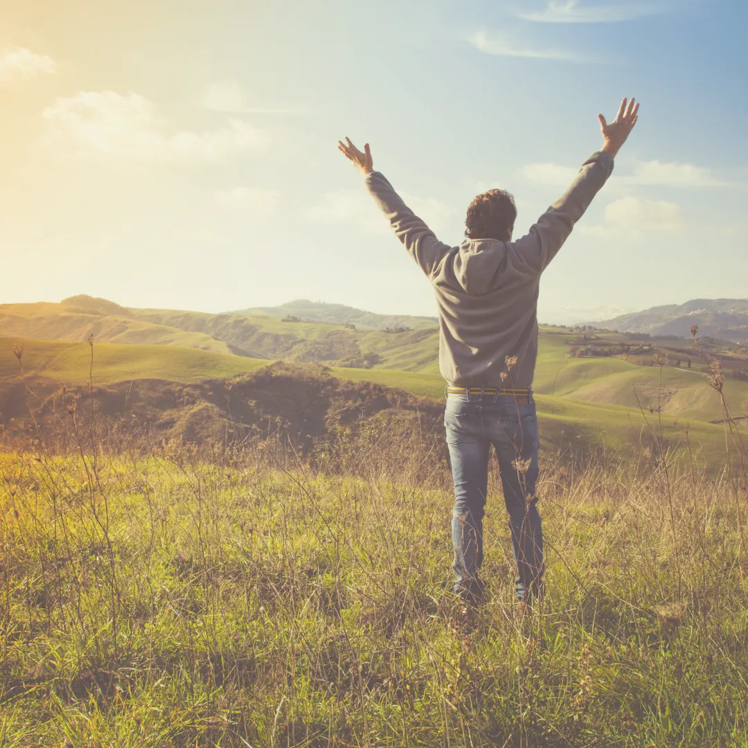 A man standing in an open field with arms raised, symbolizing renewal and energy alignment during a spring detox.