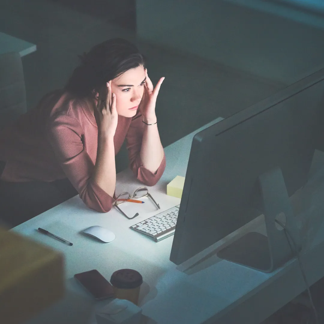 A stressed woman experiencing brain fog while working at her computer, a common symptom of a dysregulated gut-brain axis and neuroinflammation.