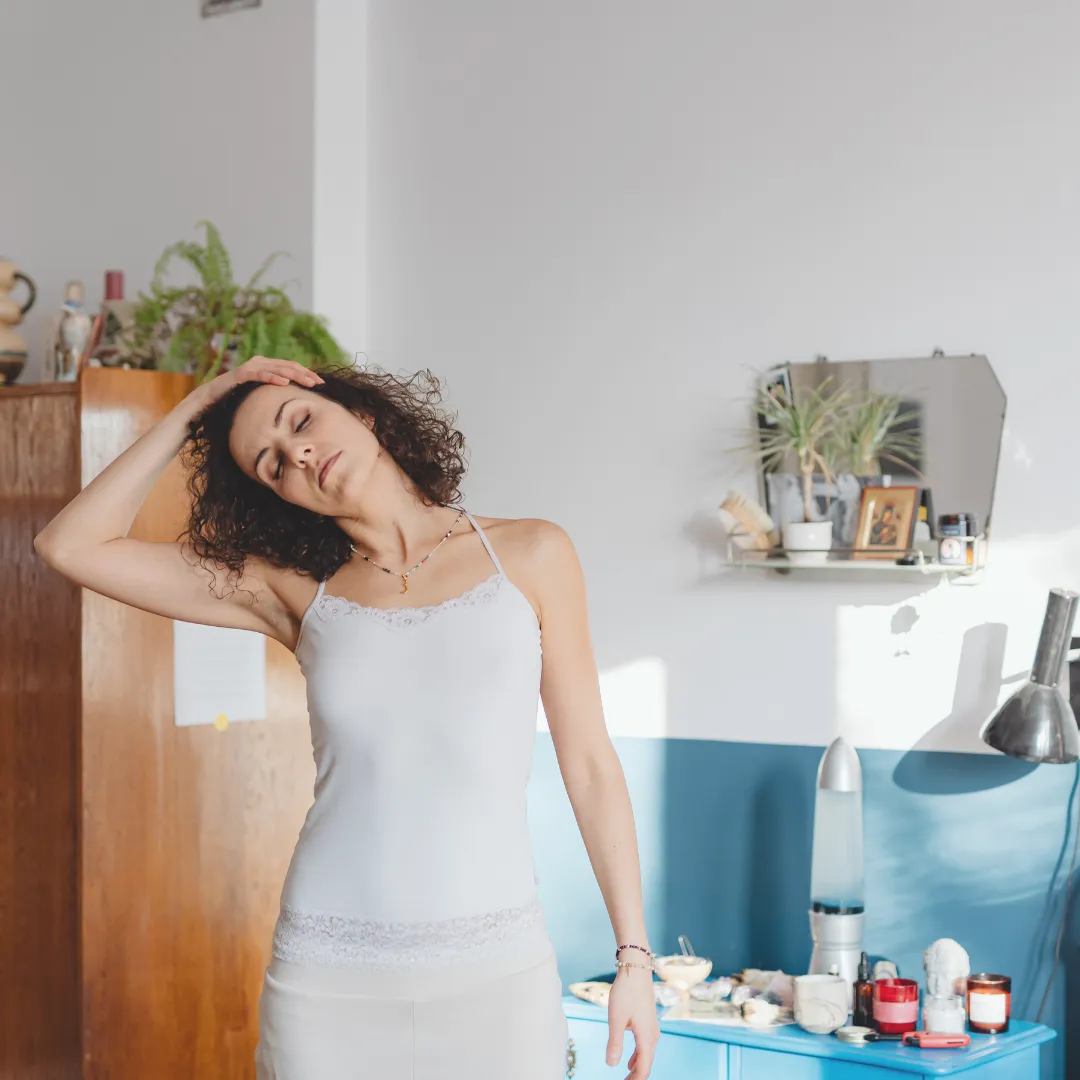 A woman gently stretching her neck, illustrating the 'gentle mobility' and 'jaw/neck release' protocol used in a taVNS "Stress-to-Sleep" evening stack to prepare the nervous system for rest.