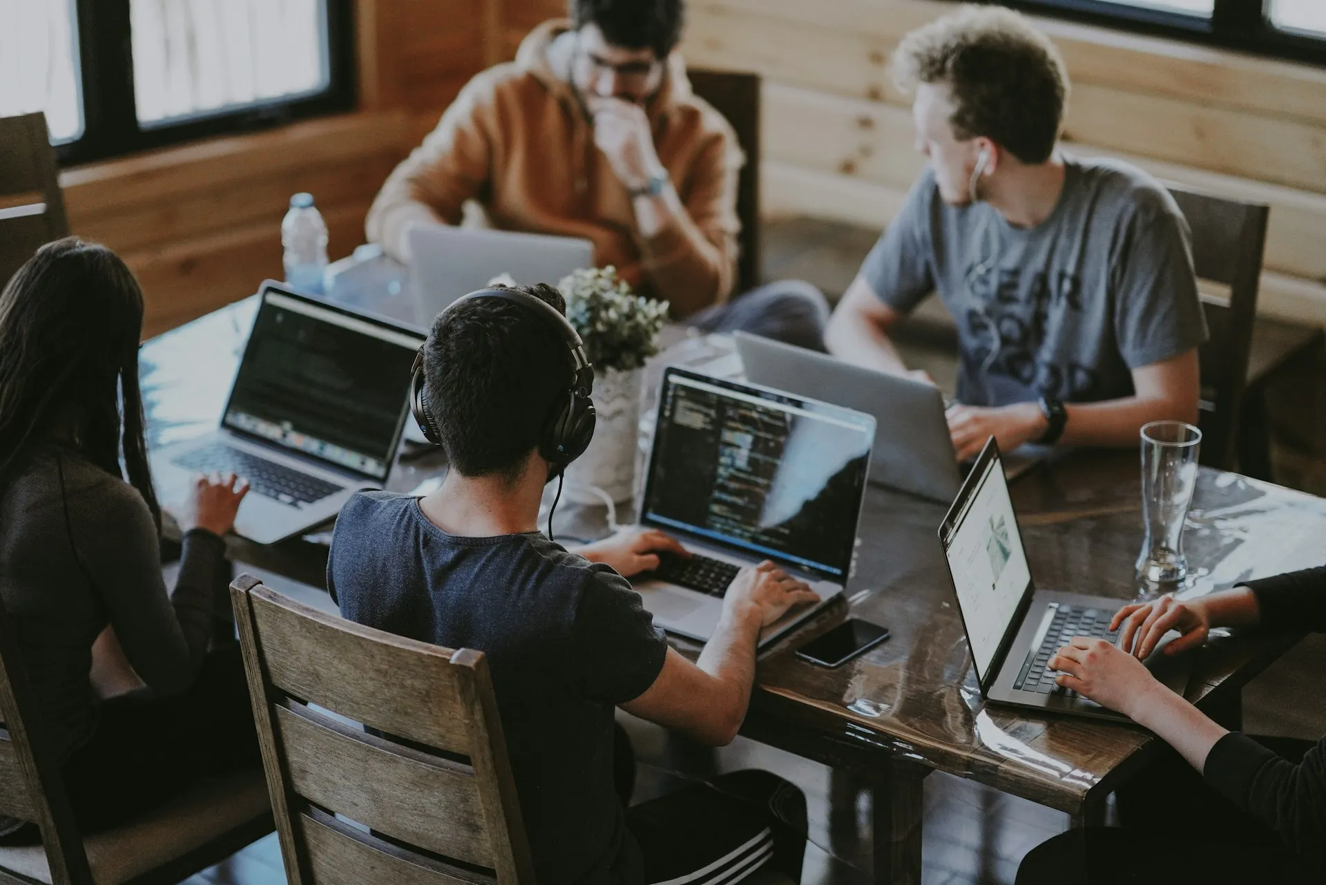 Five people working on laptops around a wooden table in a bright room