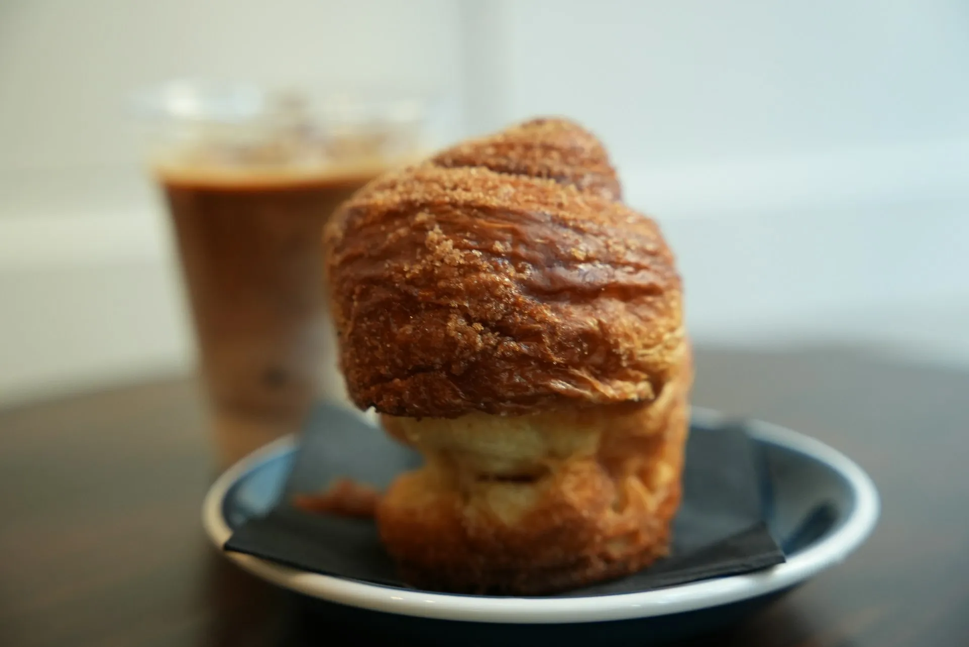 Sugar-topped croissant on a plate with an iced coffee blurred behind it