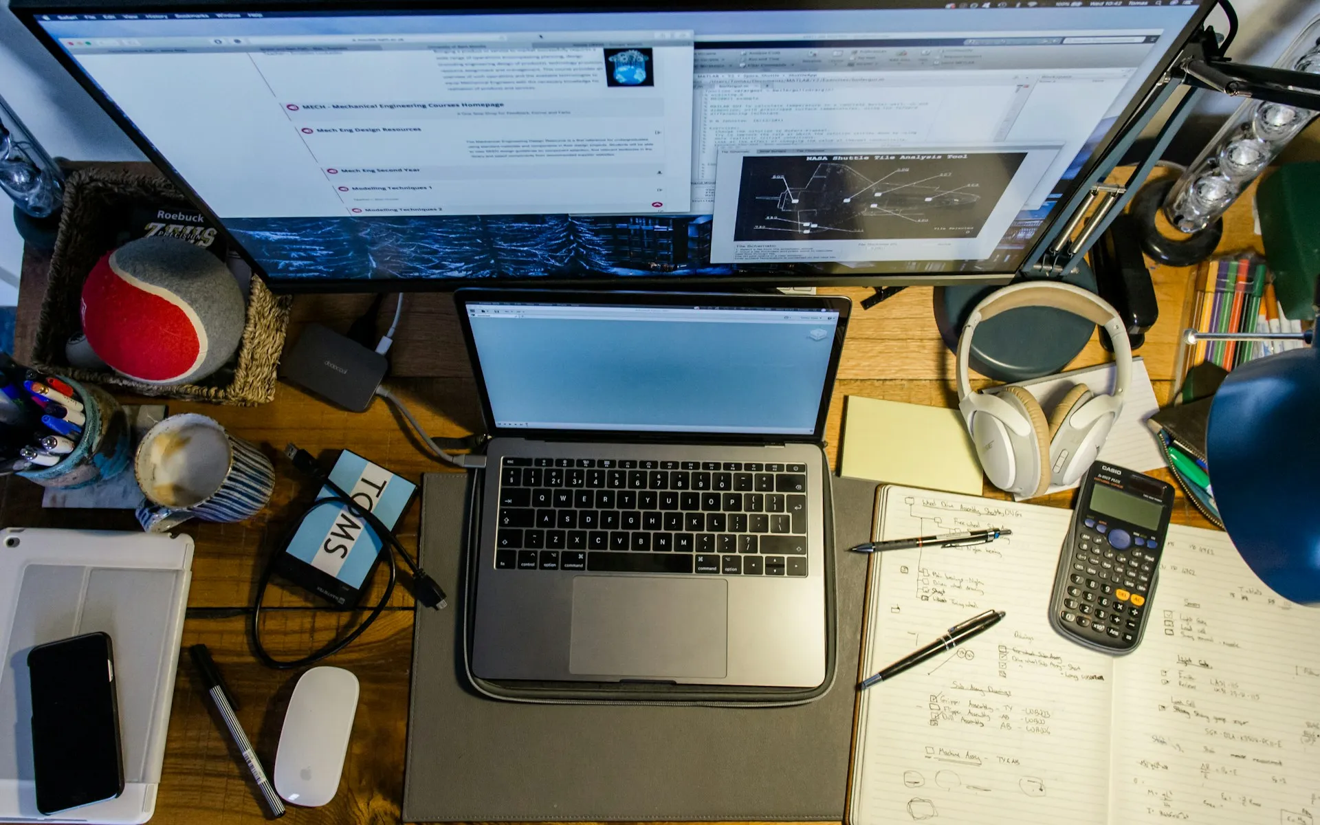 Cluttered desk with multiple screens illustrating everyday micro-stressors like notifications and multitasking.