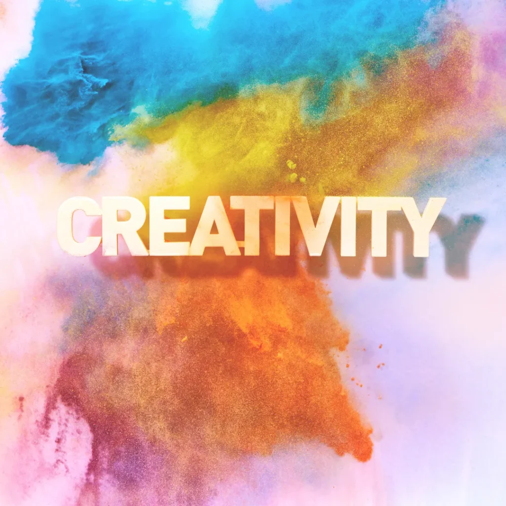 The word CREATIVITY floating in front of a vibrant explosion of blue, yellow, and orange powder, symbolizing creative energy.
