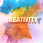 The word CREATIVITY floating in front of a vibrant explosion of blue, yellow, and orange powder, symbolizing creative energy.
