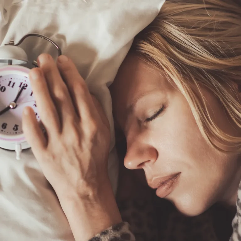 A woman sleeping peacefully next to a retro alarm clock on a pillow, illustrating the importance of aligning sleep schedules with your chronotype.