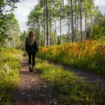 Woman walking along a narrow dirt path through aspen trees and autumn undergrowth