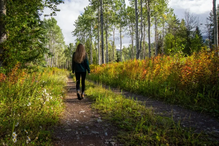 Woman walking along a narrow dirt path through aspen trees and autumn undergrowth