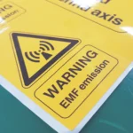 A close-up of a yellow warning label with the universal symbol for non-ionizing radiation and the words 'WARNING EMF emission'.