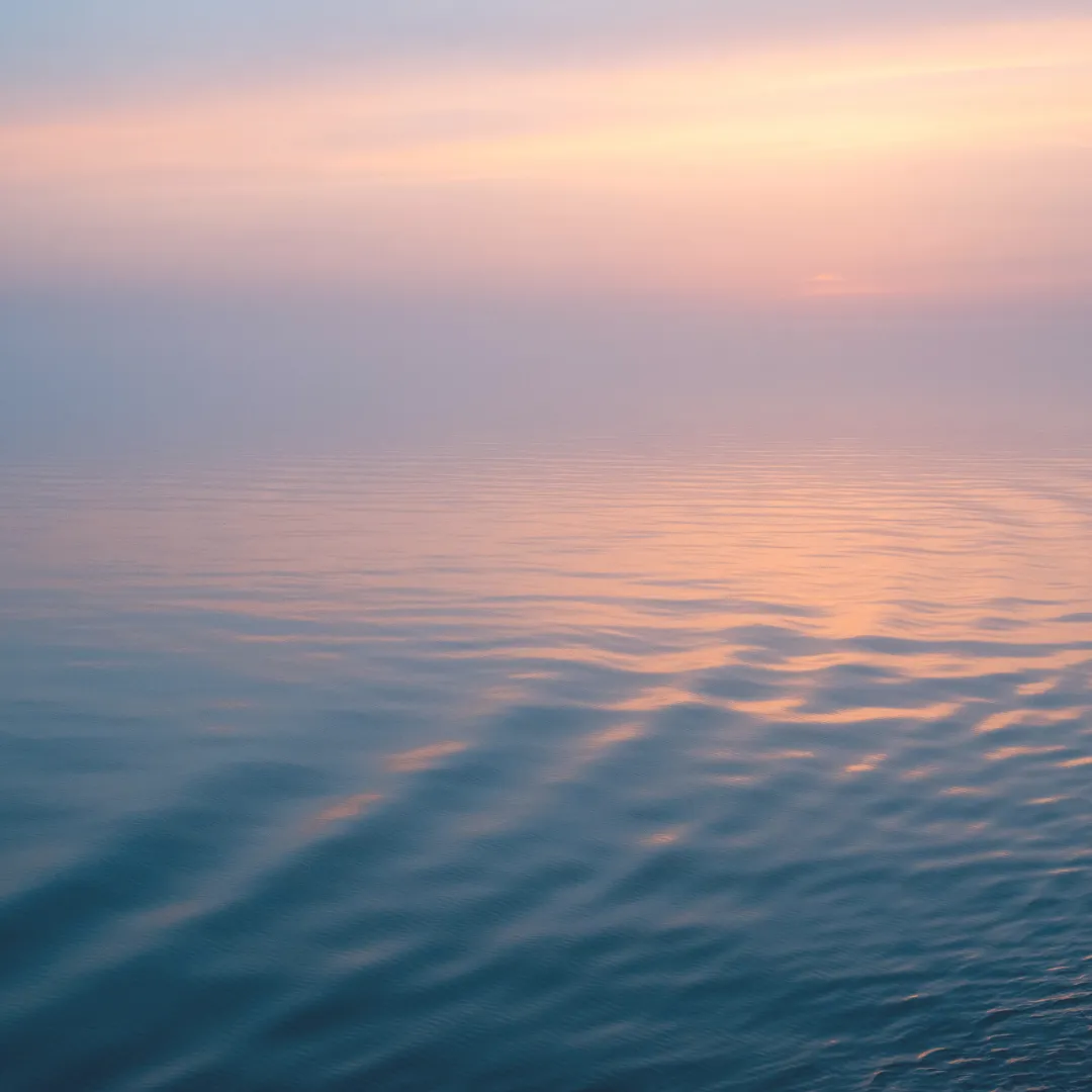 Calm ocean ripples reflecting a serene pink and orange sunset, representing the water element's connection to emotional flow, intuition, and energetic harmony.