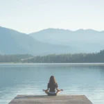 Woman meditating on a wooden dock by a serene lake at a wellness retreat.