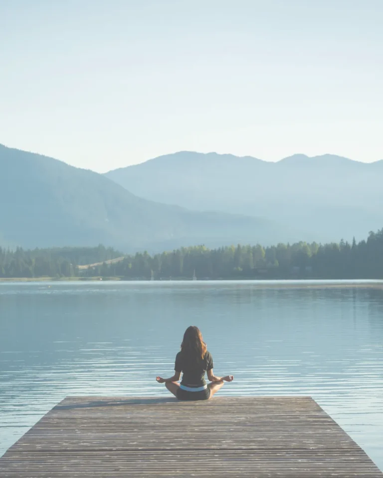 Woman meditating on a wooden dock by a serene lake at a wellness retreat.