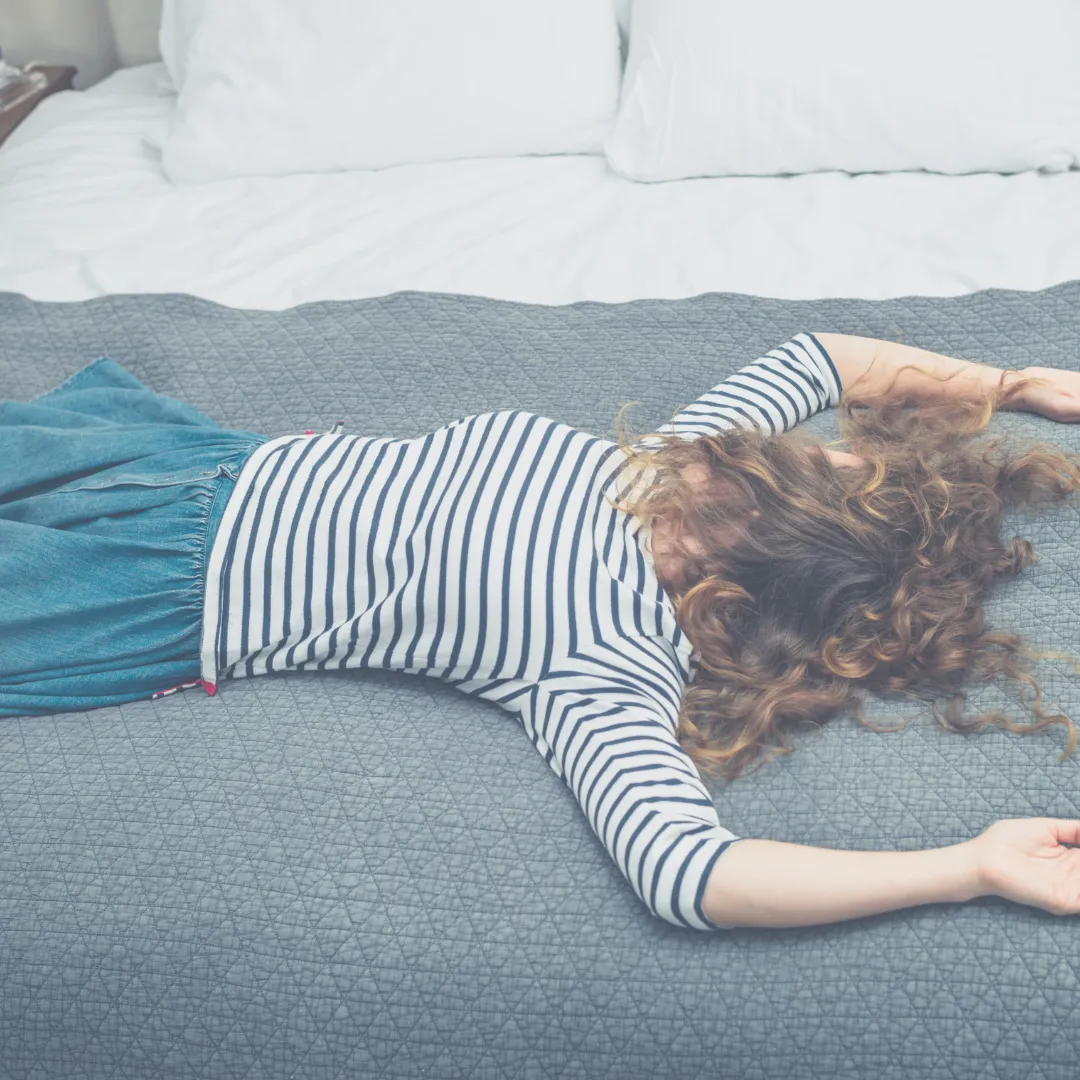 A frustrated woman lies wide awake on her bed, illustrating how an energetic imbalance or a disrupted biofield can prevent restful sleep.